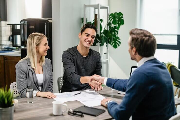 young-happy-couple-making-agreement-with-their-financial-advisor-home-men-are-shaking-hands_637285-3839